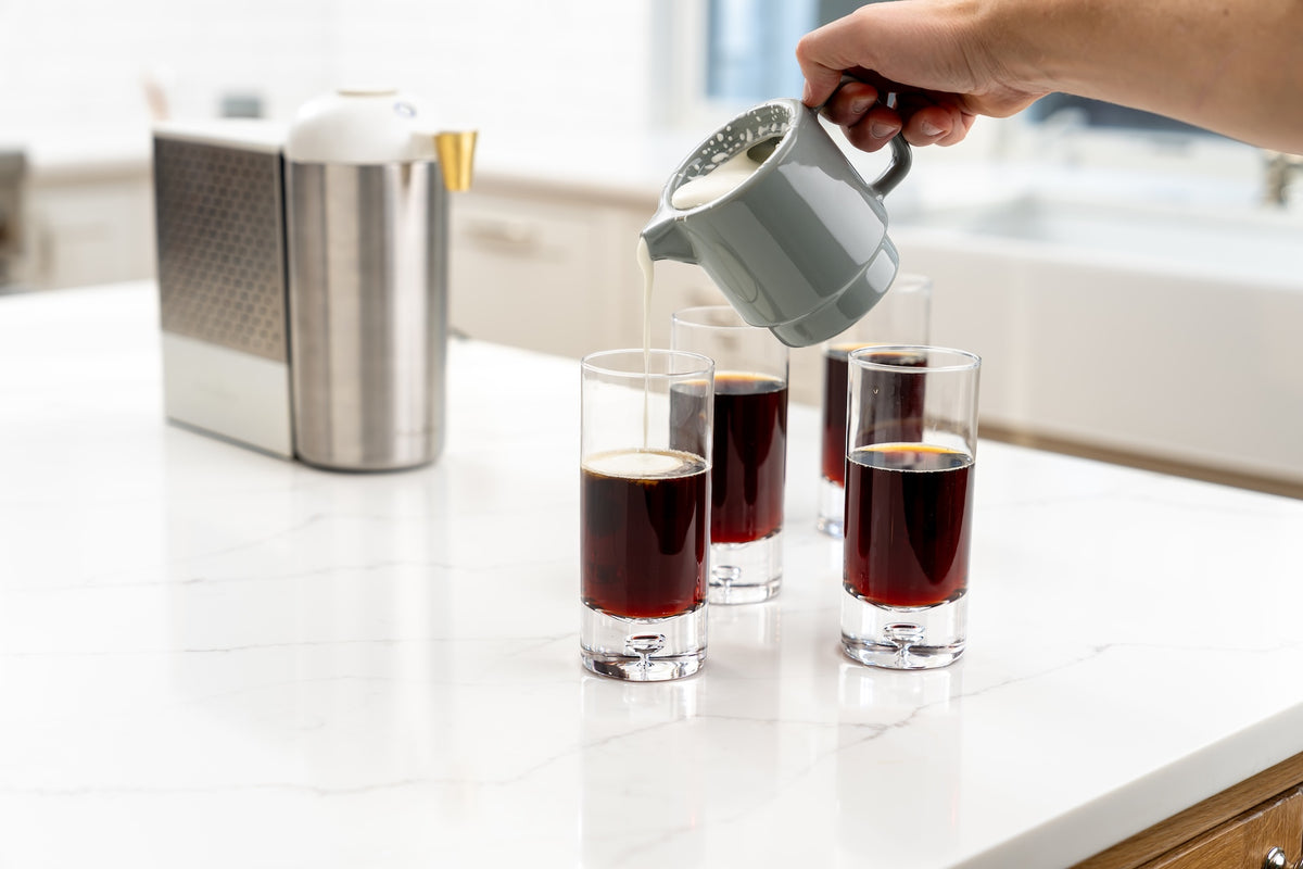 Milk being poured into a glass of cold brew beside the AstroBrew machine