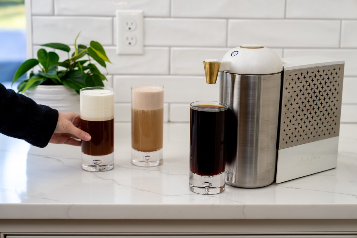 Glasses of cold brew and creamy coffee beside an AstroBrew machine